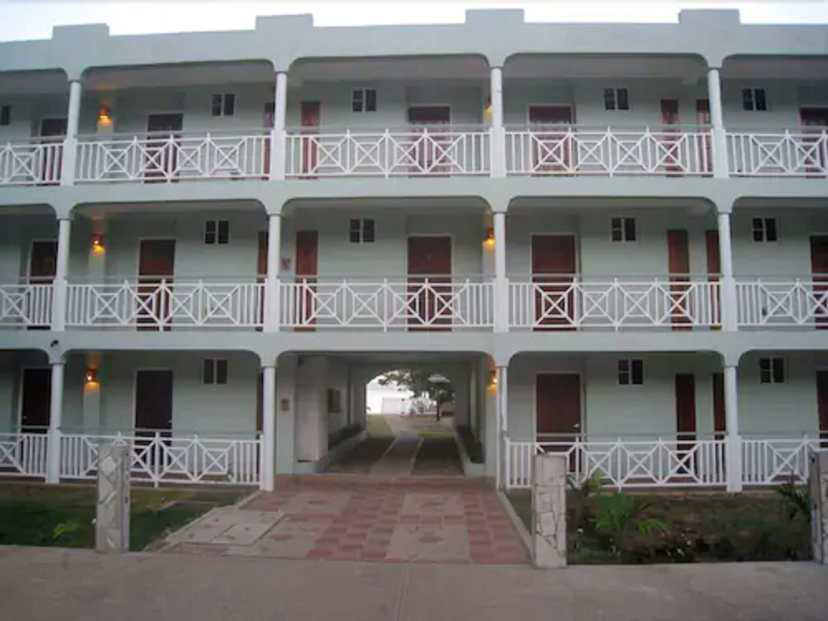 A multi-story hotel with a central corridor leading to individual rooms, white railings, and a consistent architectural style.