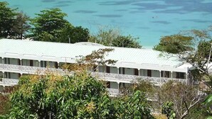 Un bâtiment situé sur la côte, avec un toit blanc et de nombreuses fenêtres, qui offre une vue sur une mer turquoise, avec un bateau visible au loin.