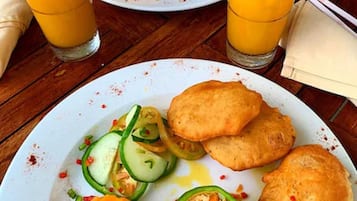 A table with a plate of food including mango slices, cucumber slices, and a stuffed vegetable, along with two glasses of orange juice.