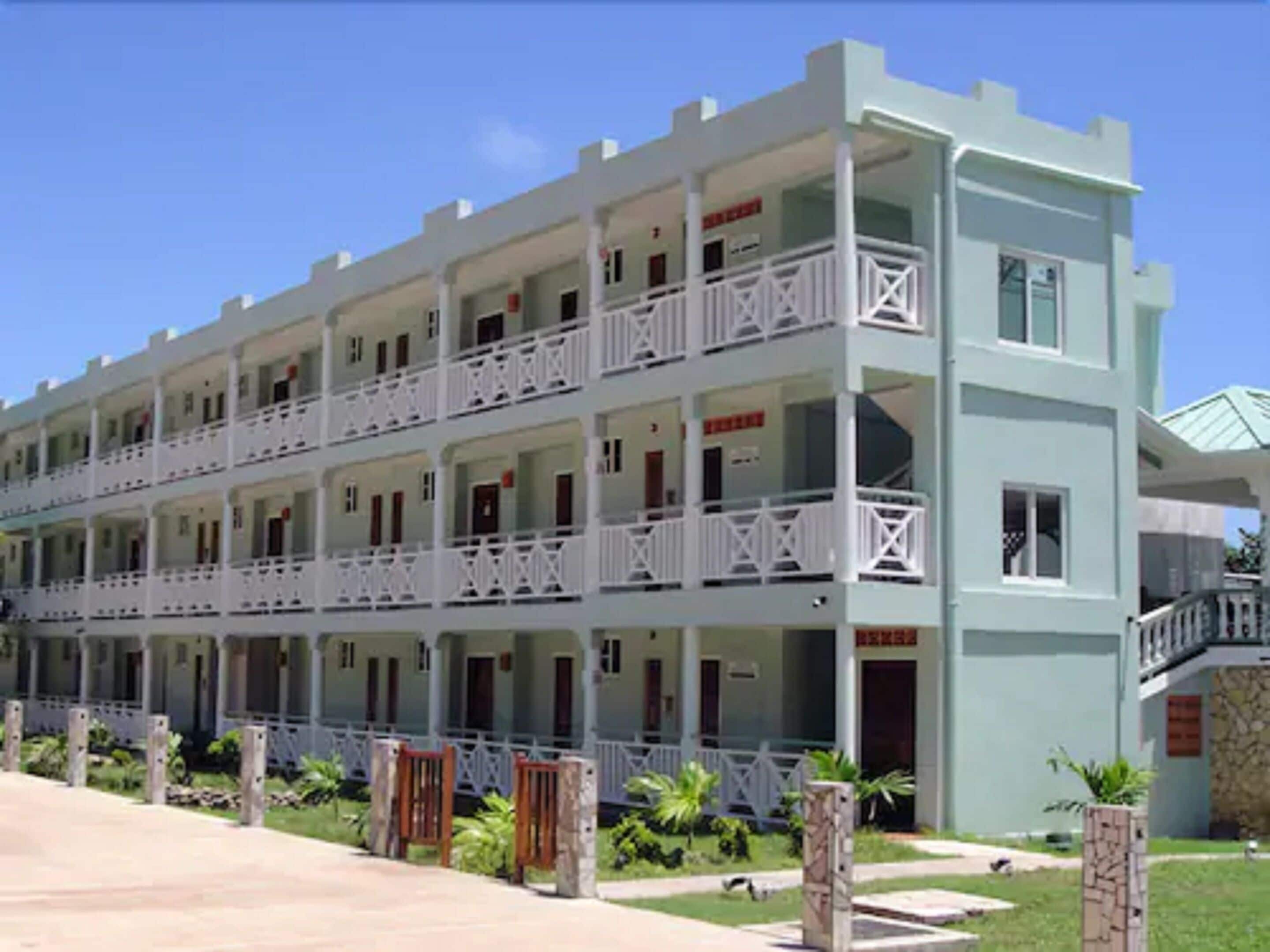 Un hotel de varios pisos con balcones, fachada de piedra y cielo azul despejado.