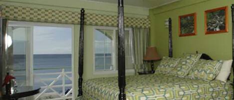 A four-poster bed with a patterned bedspread, a ceiling fan, and a view of the ocean through large windows.