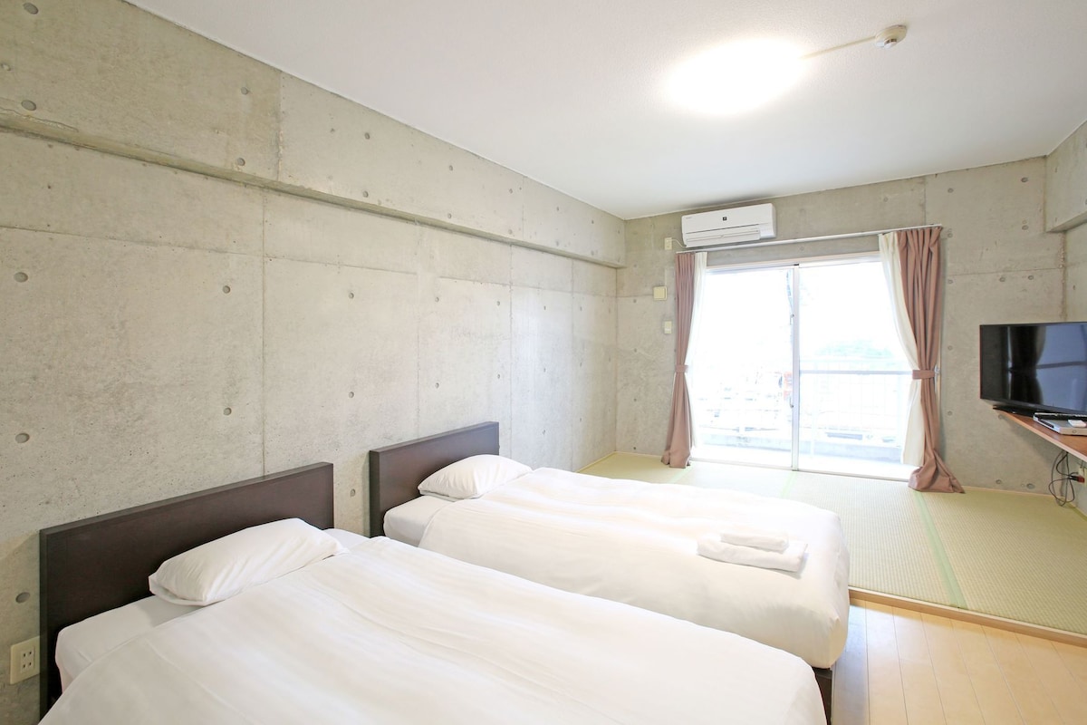 Une chambre d’hôtel avec deux lits, une télévision, un appareil de climatisation et une fenêtre avec des rideaux.
