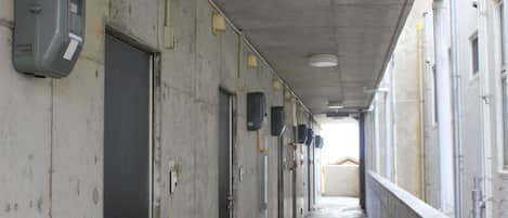A long, narrow corridor with doors on both sides, overhead pipes, and a concrete ceiling.