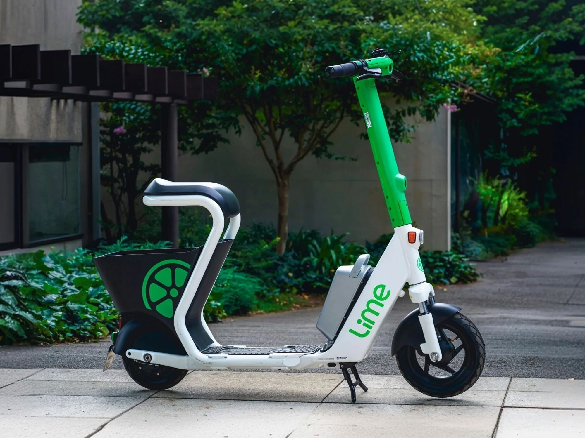 A lime green and white electric scooter with a basket, parked on a sidewalk.