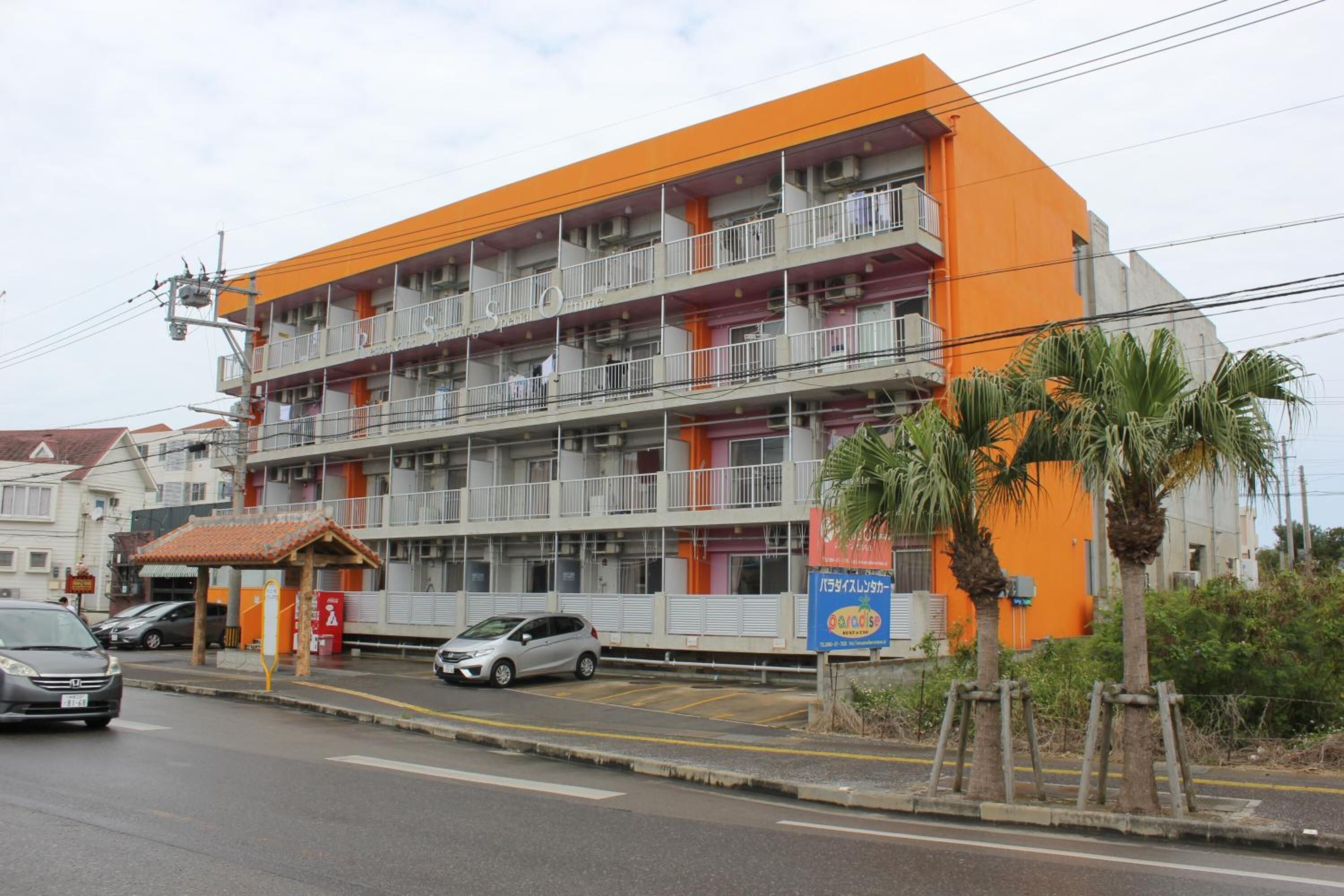 A multi-story hotel with balconies, a covered entrance, and a parking area.