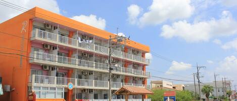 Un edificio de varios pisos con balcones, una zona de estar al aire libre techada y un cielo despejado.