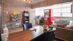 Un espacio de oficina moderno con una mesa de conferencias de madera, sillas negras, un sofá y una máquina expendedora roja.