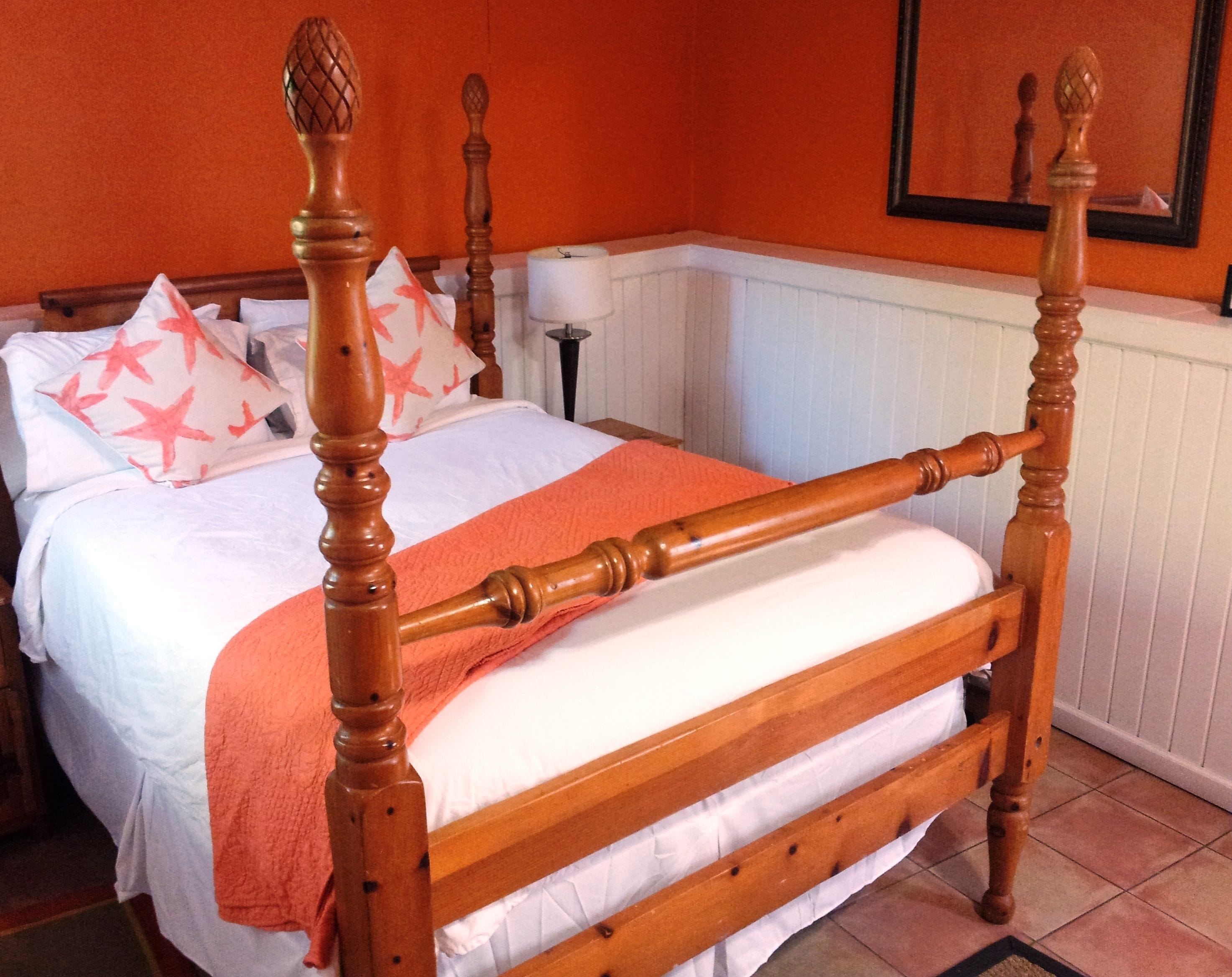 Una cama con dosel, con cubrecama blanco y naranja, cabecera de madera y almohadas a juego.