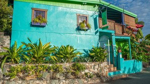 A turquoise building with two windows, a stone wall, and a staircase leading to a porch. - St John Inn (St. John)