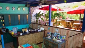 An outdoor bar area with wooden furniture, a counter with various items, and red umbrellas. - St John Inn (St. John)