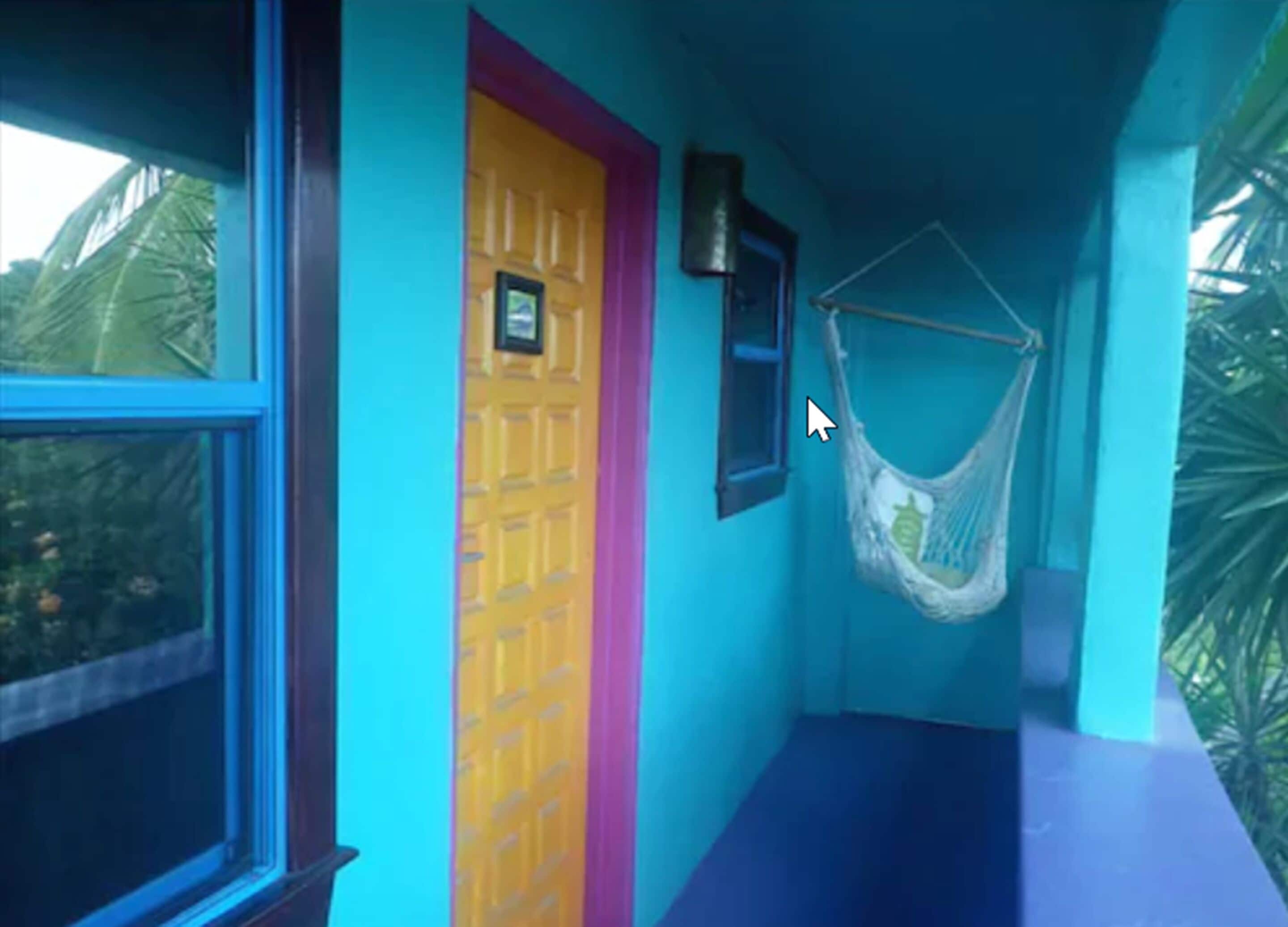 Un pasillo estrecho con una puerta amarilla, una hamaca y una ventana.