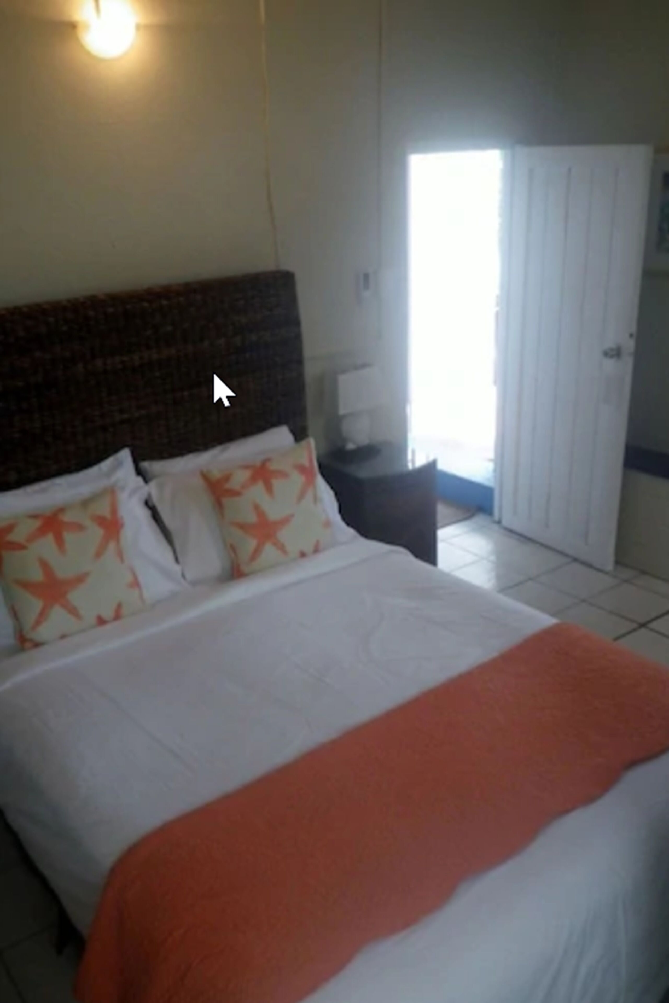 Quarto de hotel com uma cama grande, uma mesa de cabeceira, uma luminária e uma porta que dá para uma varanda.