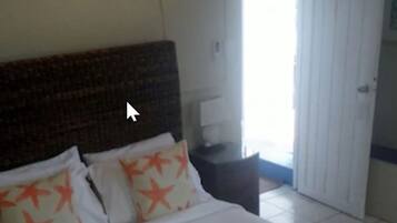 Quarto de hotel com uma cama grande, uma mesa de cabeceira, uma luminária e uma porta que dá para uma varanda.