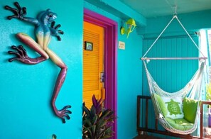 A vibrant room with a colorful frog decoration, a bright yellow door, and a hammock chair with green cushions.