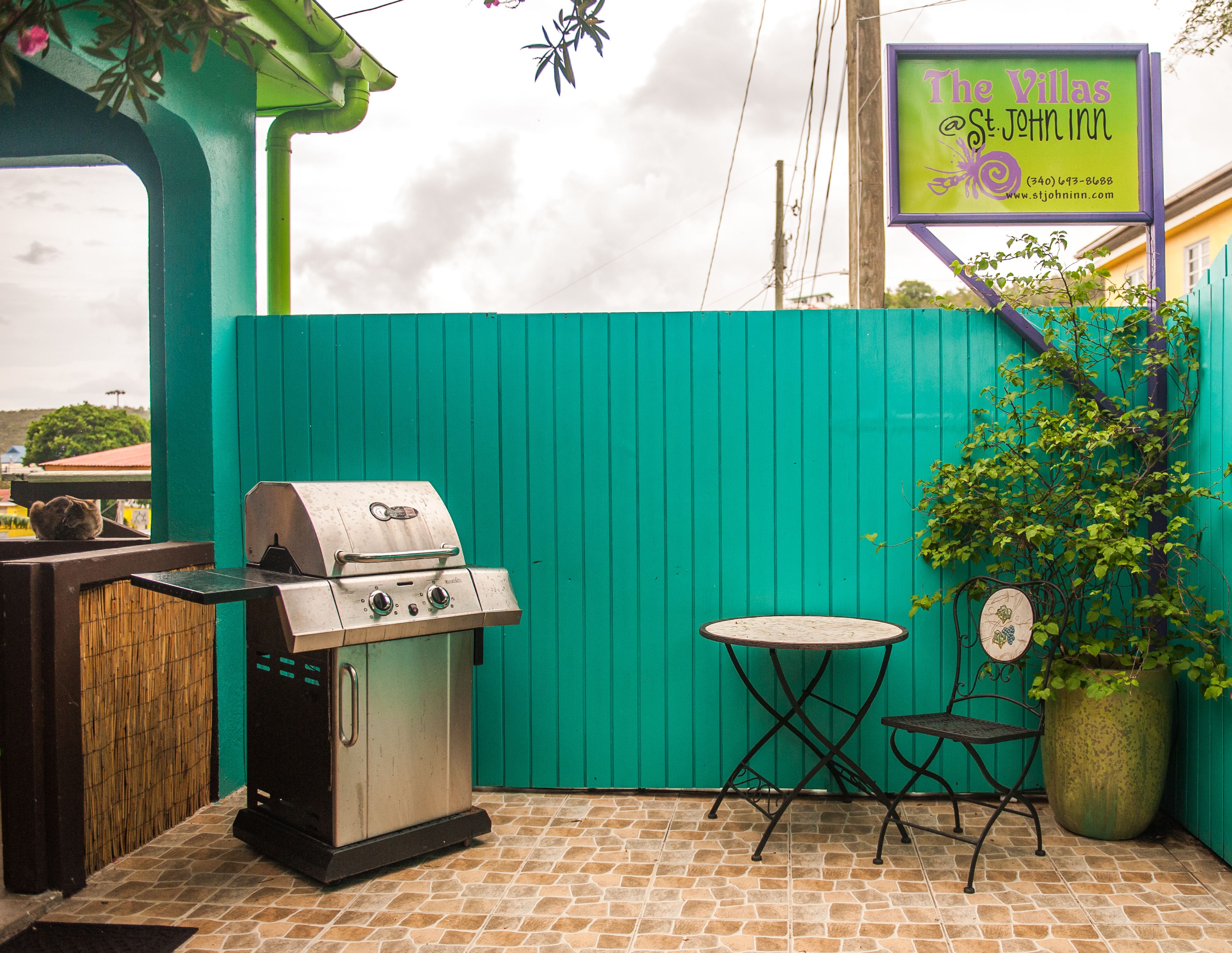 An outdoor patio with a grill, a table, and chairs, a potted plant, and a sign for The Villas St. John Inn.