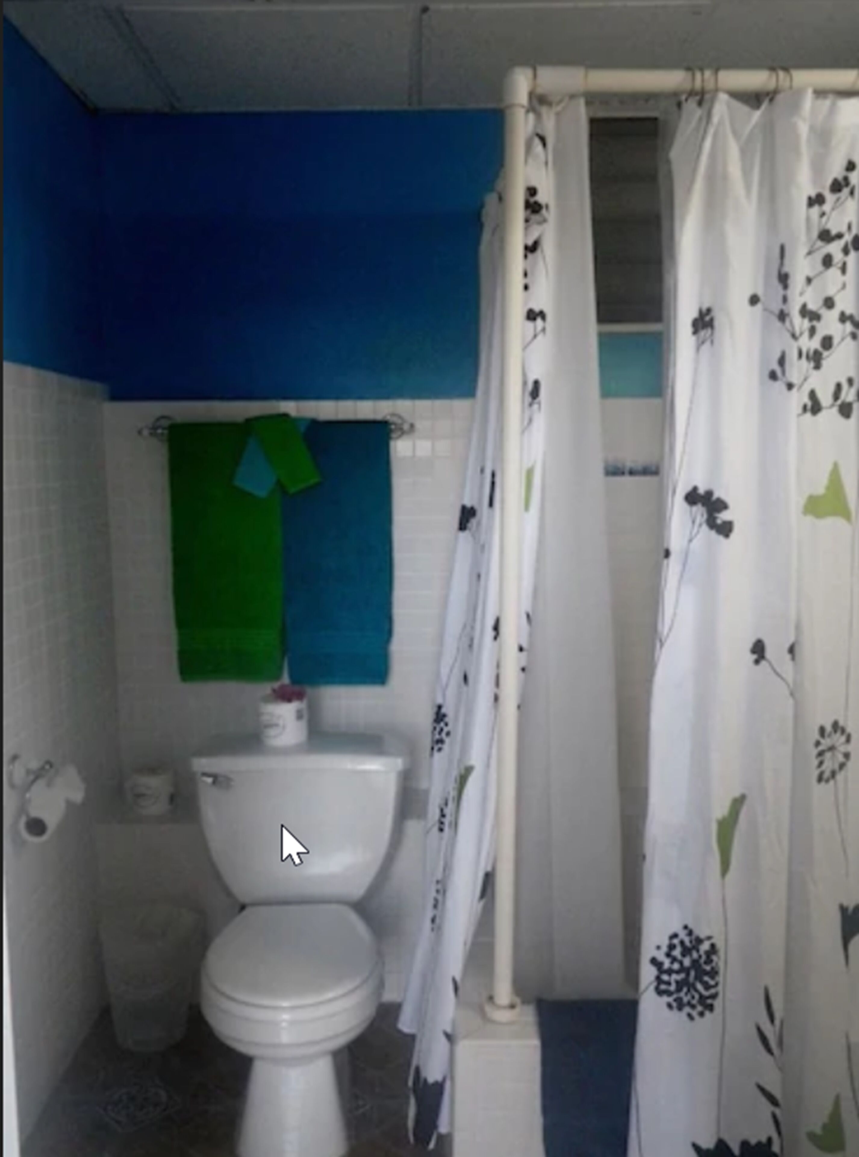 A small bathroom with a toilet, a green towel hanging on the wall, and a shower curtain with a floral pattern.