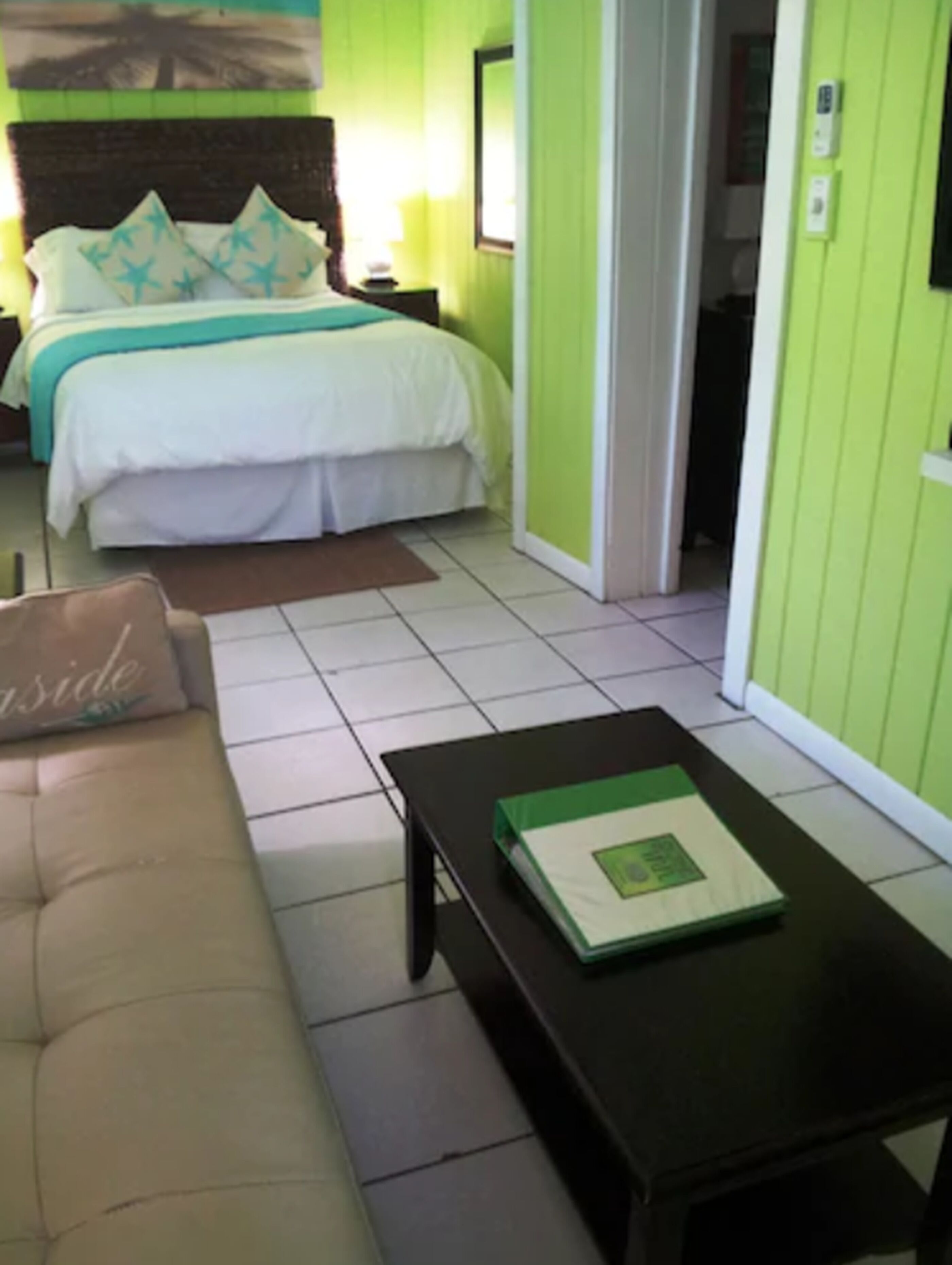 A bedroom with a bed, a nightstand, a green wall, a window, and a door.