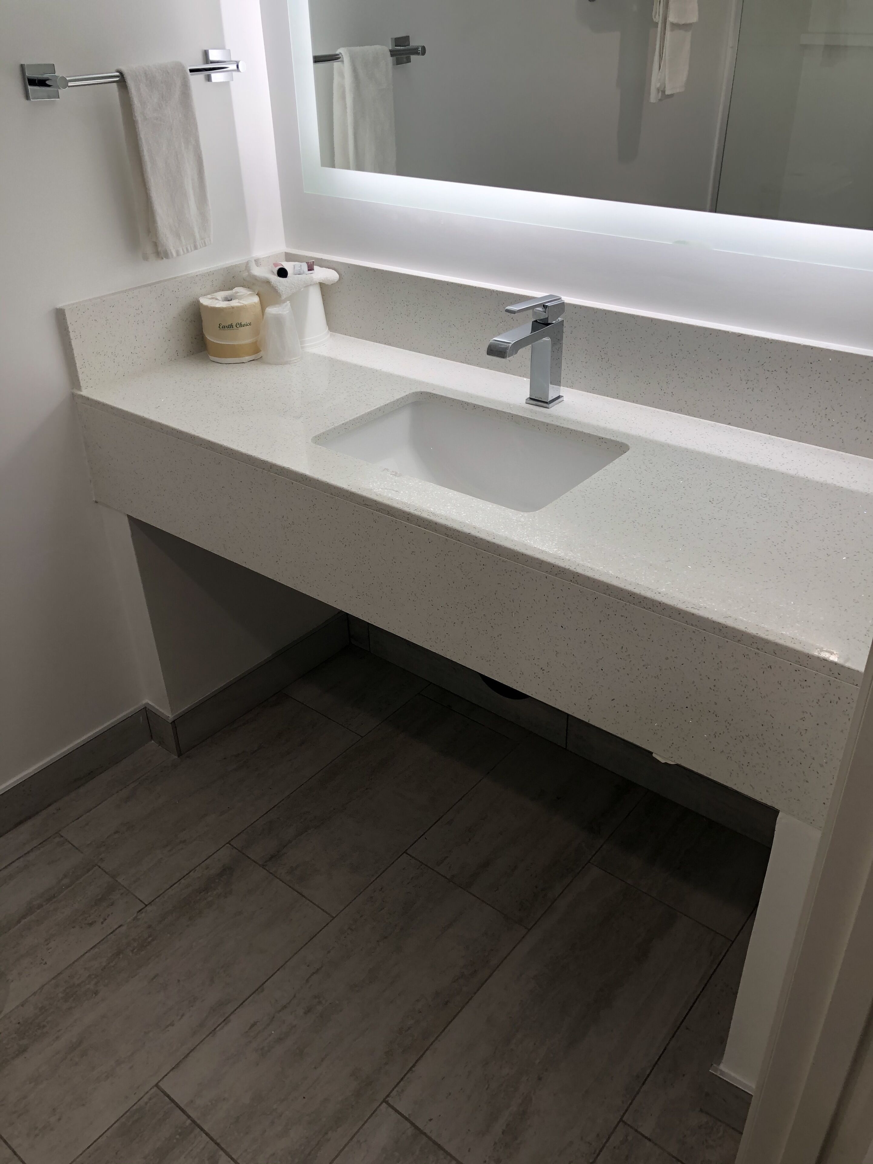 Un baño con encimera blanca con motas, un lavabo rectangular, un espejo y un perchero para toallas.