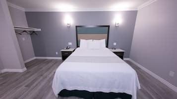 A neatly made bed in a hotel room with a grey wall, a wooden floor, and a headboard with a blue panel.