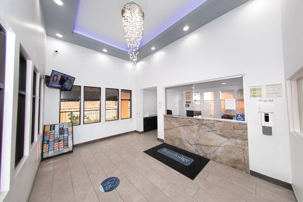A reception area with a marble counter, a chandelier, a TV screen, and a reception desk.
