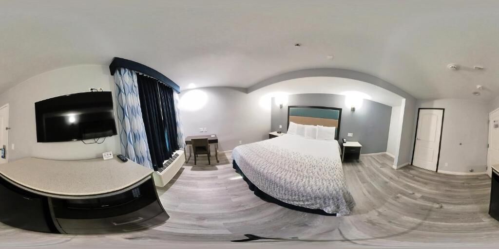 A panoramic view of a hotel room with a curved ceiling, a bed, a desk, a chair, a TV, and a bathroom.
