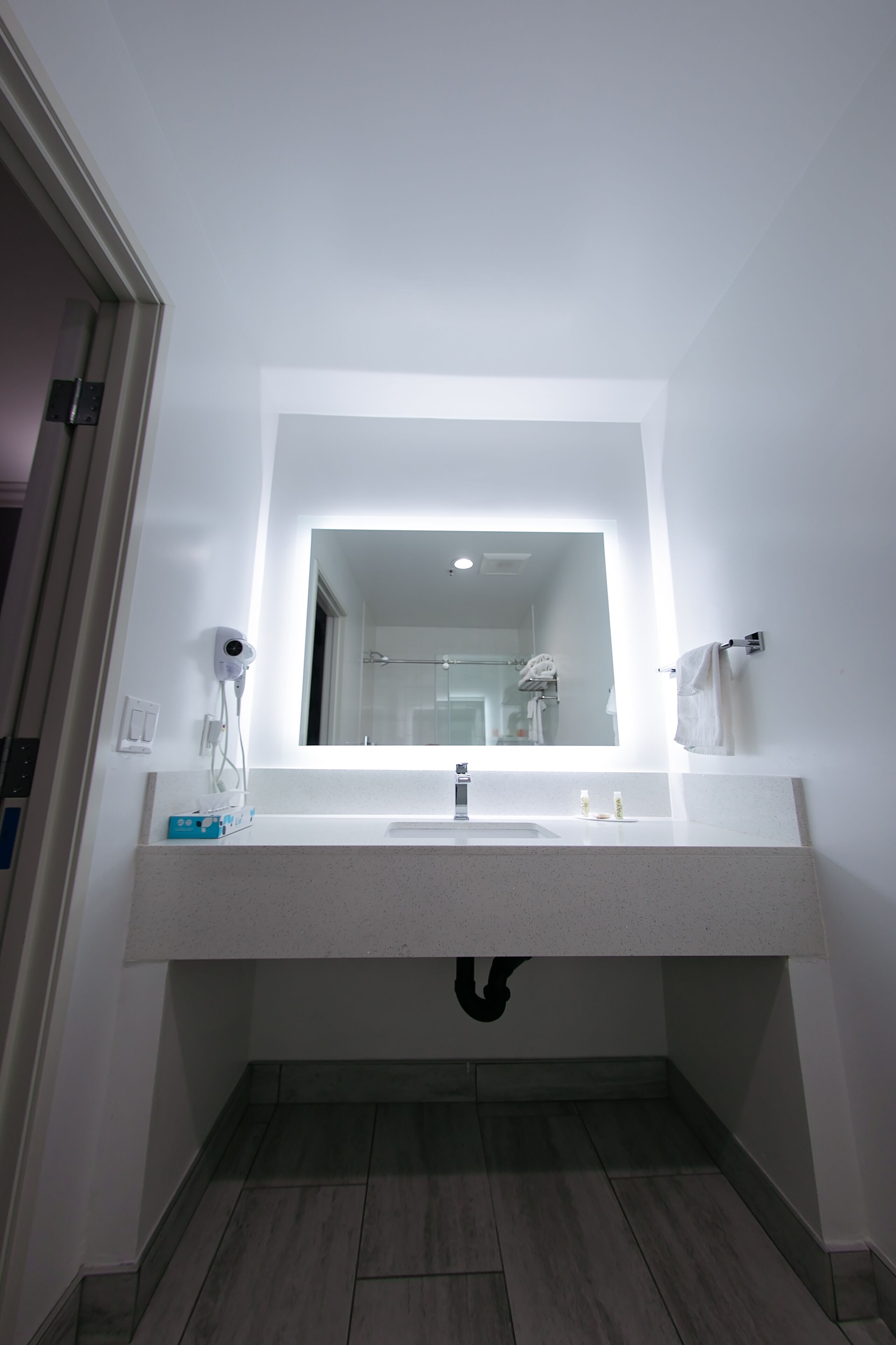 Un baño moderno con un espejo grande, lavamanos blanco y un perchero para toallas.