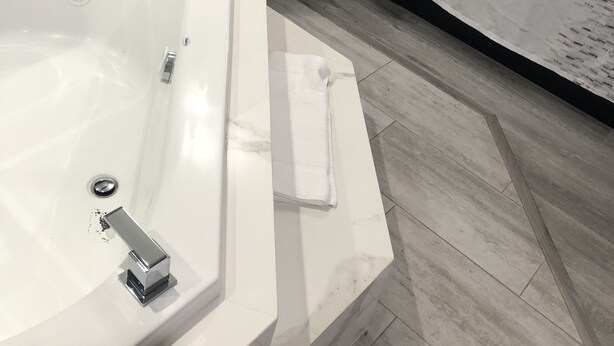 Ein modernes Hotelzimmer mit einer großzügigen Badewanne, einem Nachttisch mit Lampe und einem ordentlich bezogenen Bett.