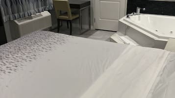 Habitación de hotel con cama, escritorio, silla, radiador y bañera.