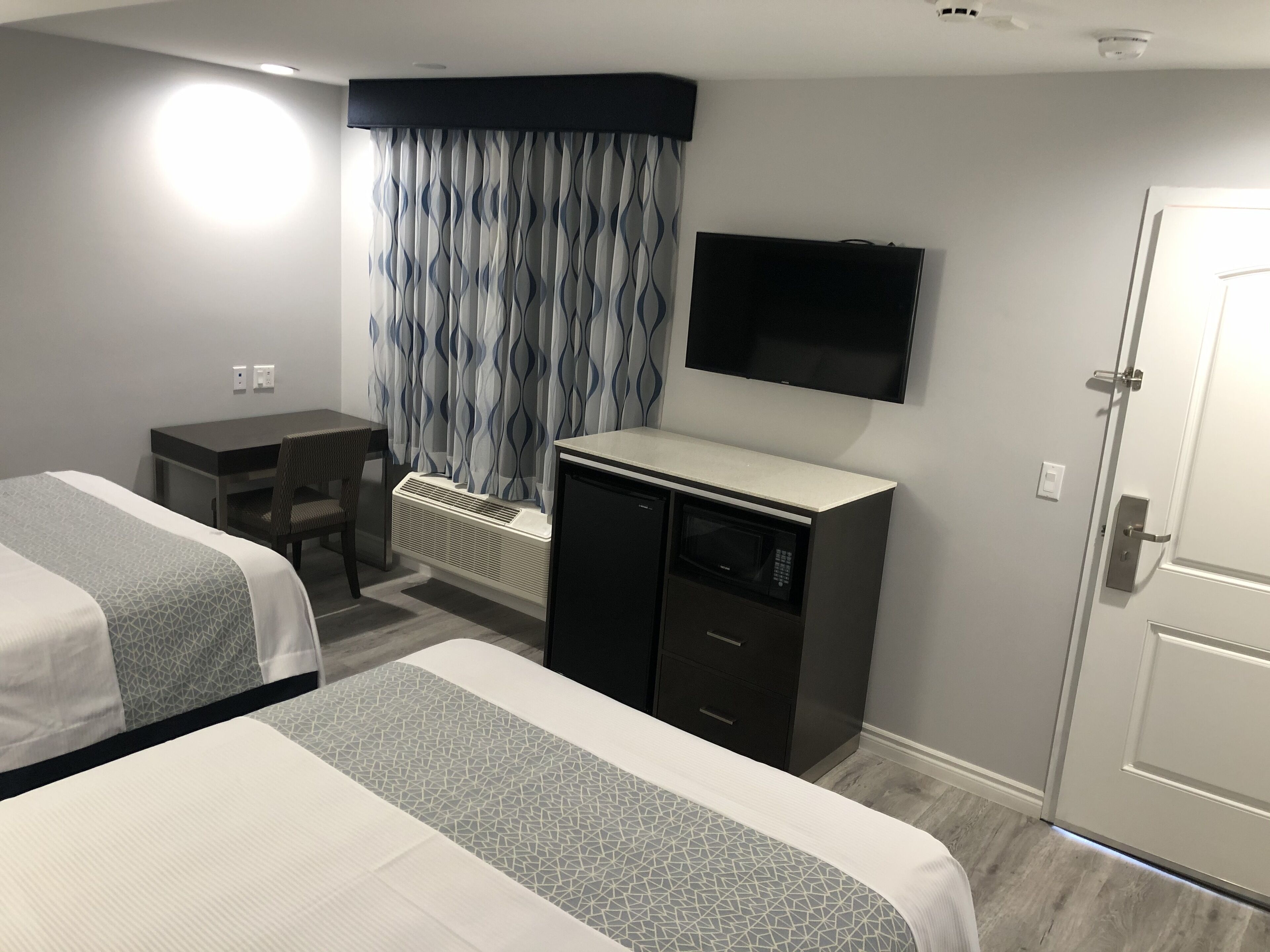 A hotel room with two beds, a desk, a television, and a minibar.
