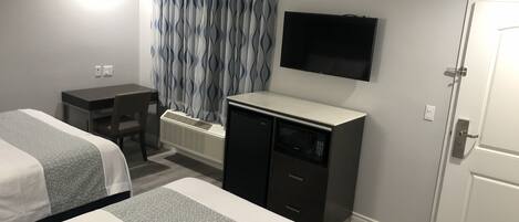 A hotel room with two beds, a desk, a television, and a minibar.