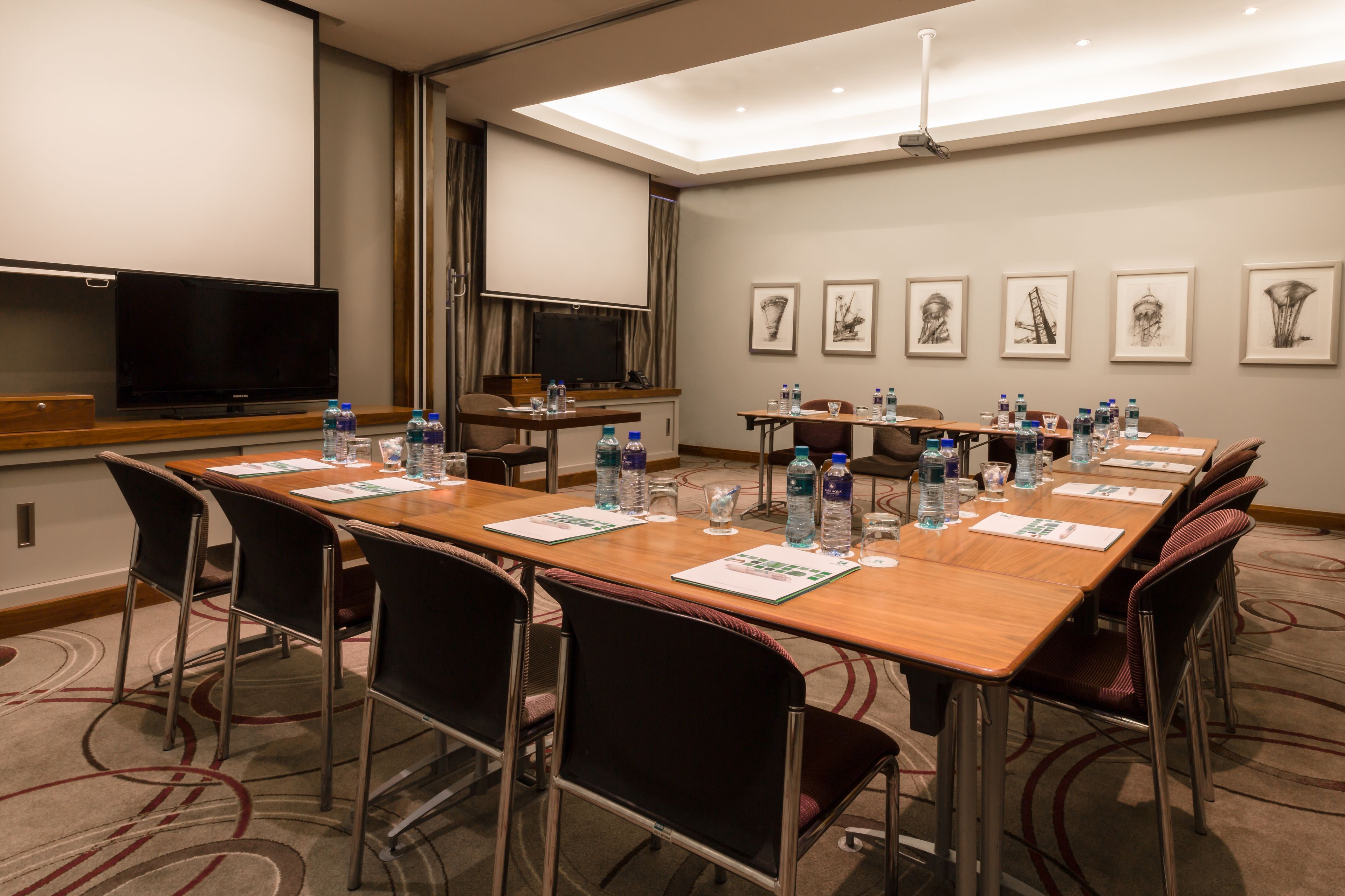 Ein Konferenzraum mit langem Tisch, Stühlen, Wasserflaschen und einer Projektionsleinwand.