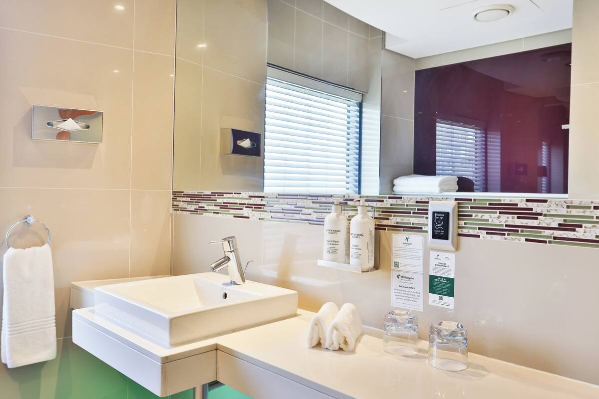 Ein modernes Badezimmer mit einem großen Waschbecken, einem Spiegel und einem Fenster mit Jalousien.