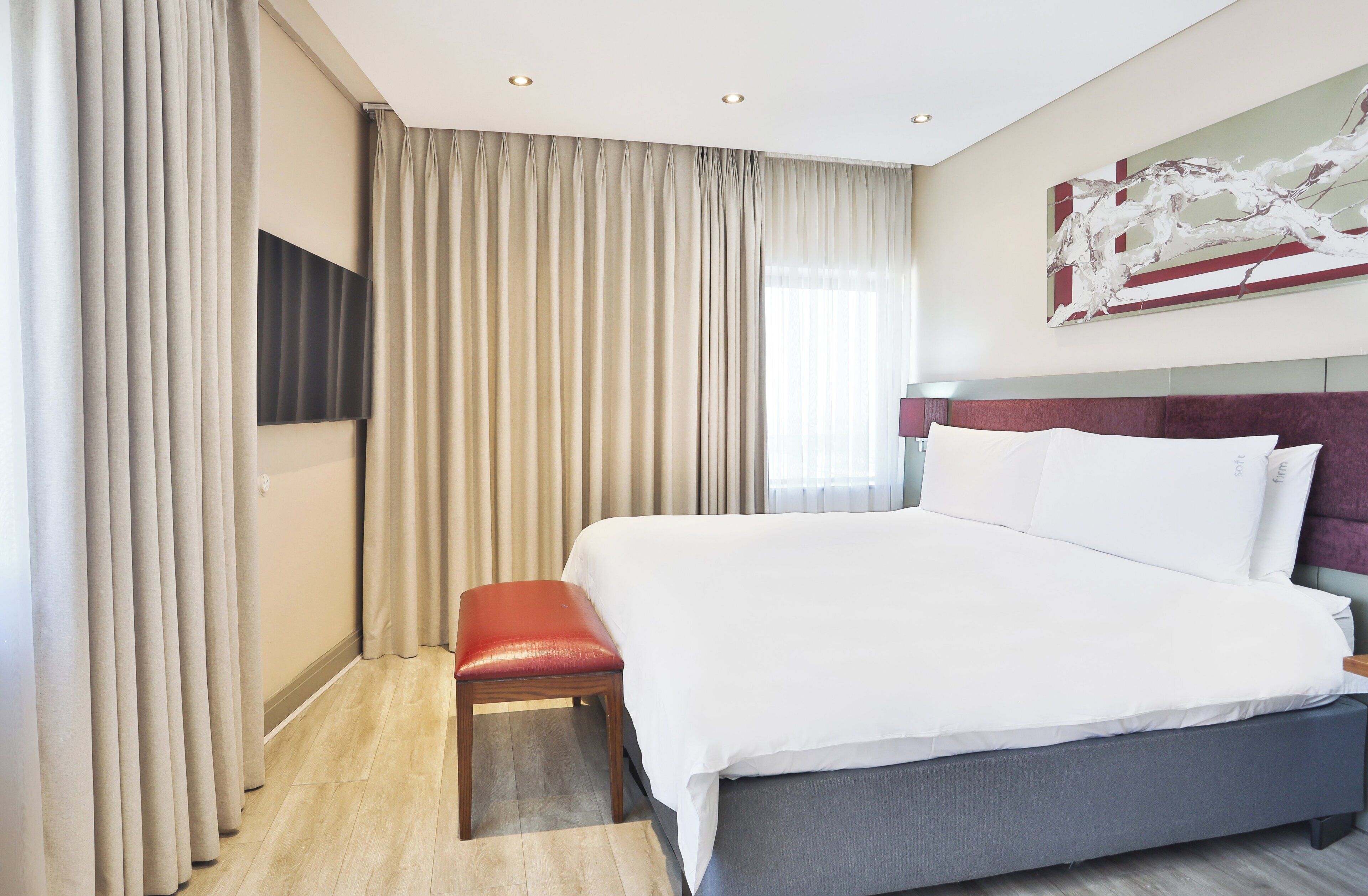 Een hotelkamer met een groot bed, een rode bank, een flatscreen televisie en een modern abstract schilderij aan de muur.