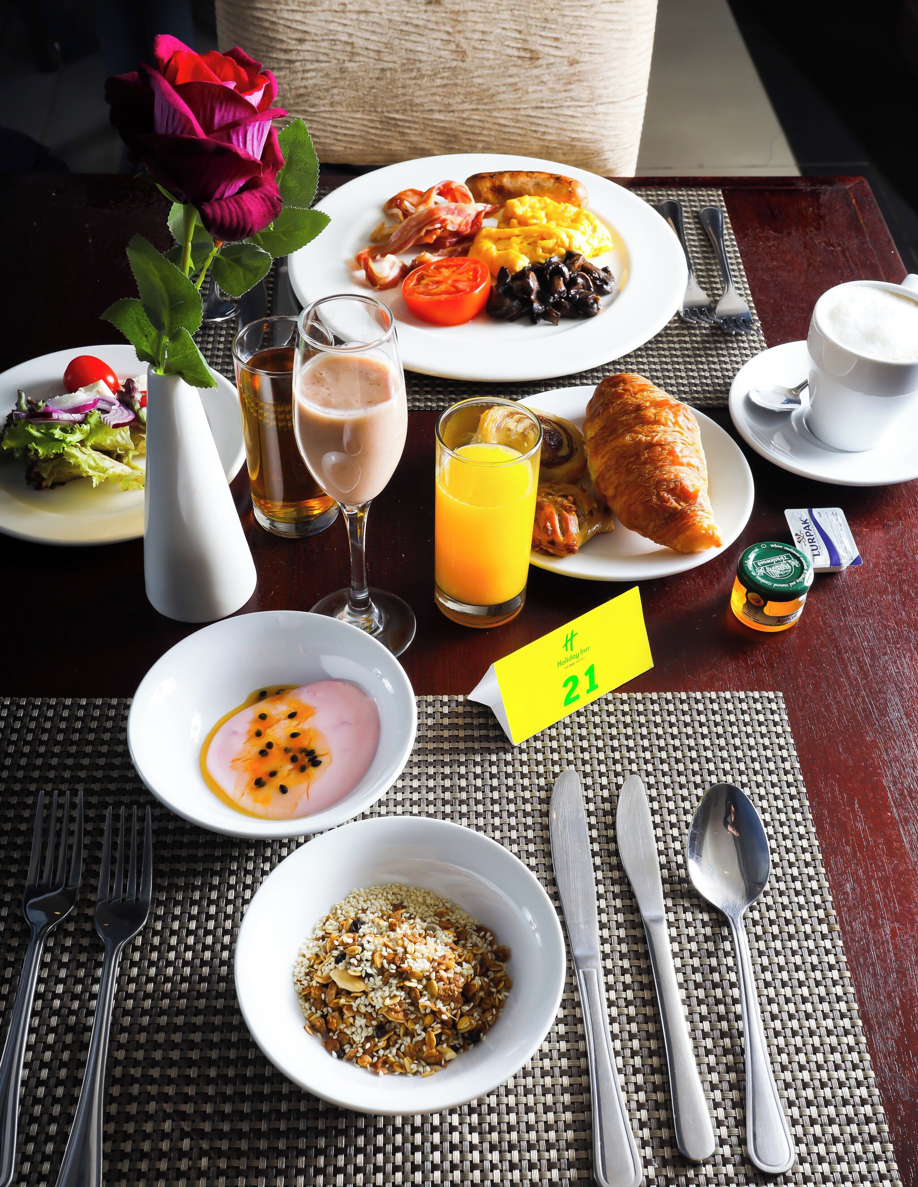 A breakfast setting with plates of food, a vase with a rose, a glass of orange juice, and a table with a placemat.
