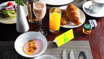 A breakfast setting with plates of food, a vase with a rose, a glass of orange juice, and a table with a placemat.