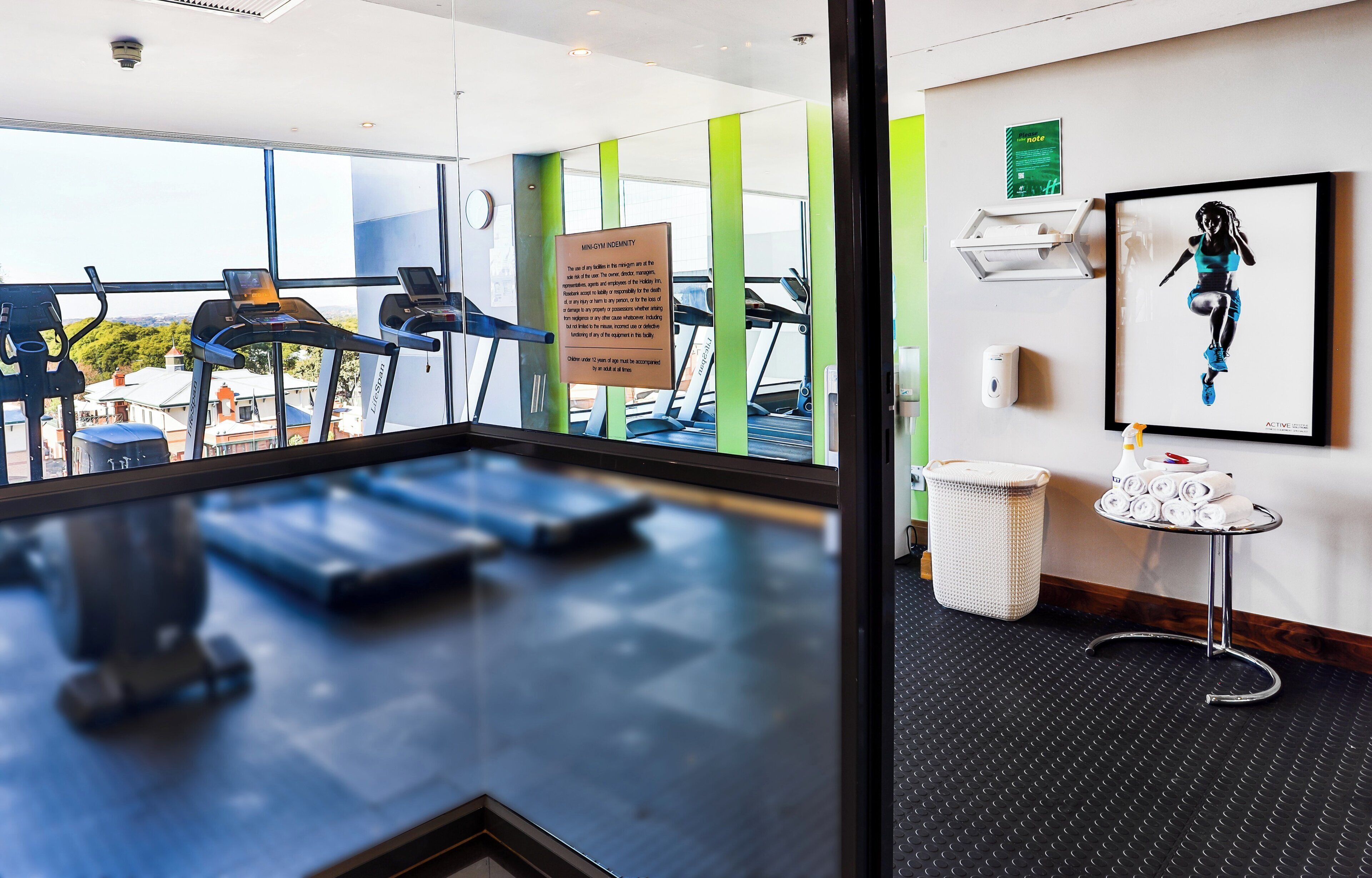 Ein Fitnessraum mit Laufbändern, einem Schild, einem gerahmten Bild und einem kleinen Tisch mit Handtüchern.