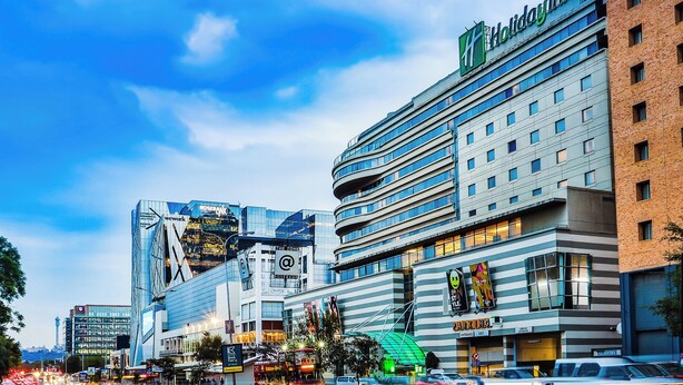 A Holiday Inn hotel with a modern design, featuring multiple floors and a prominent curved structure. - Holiday Inn Johannesburg - Rosebank by IHG (Johannesburg)