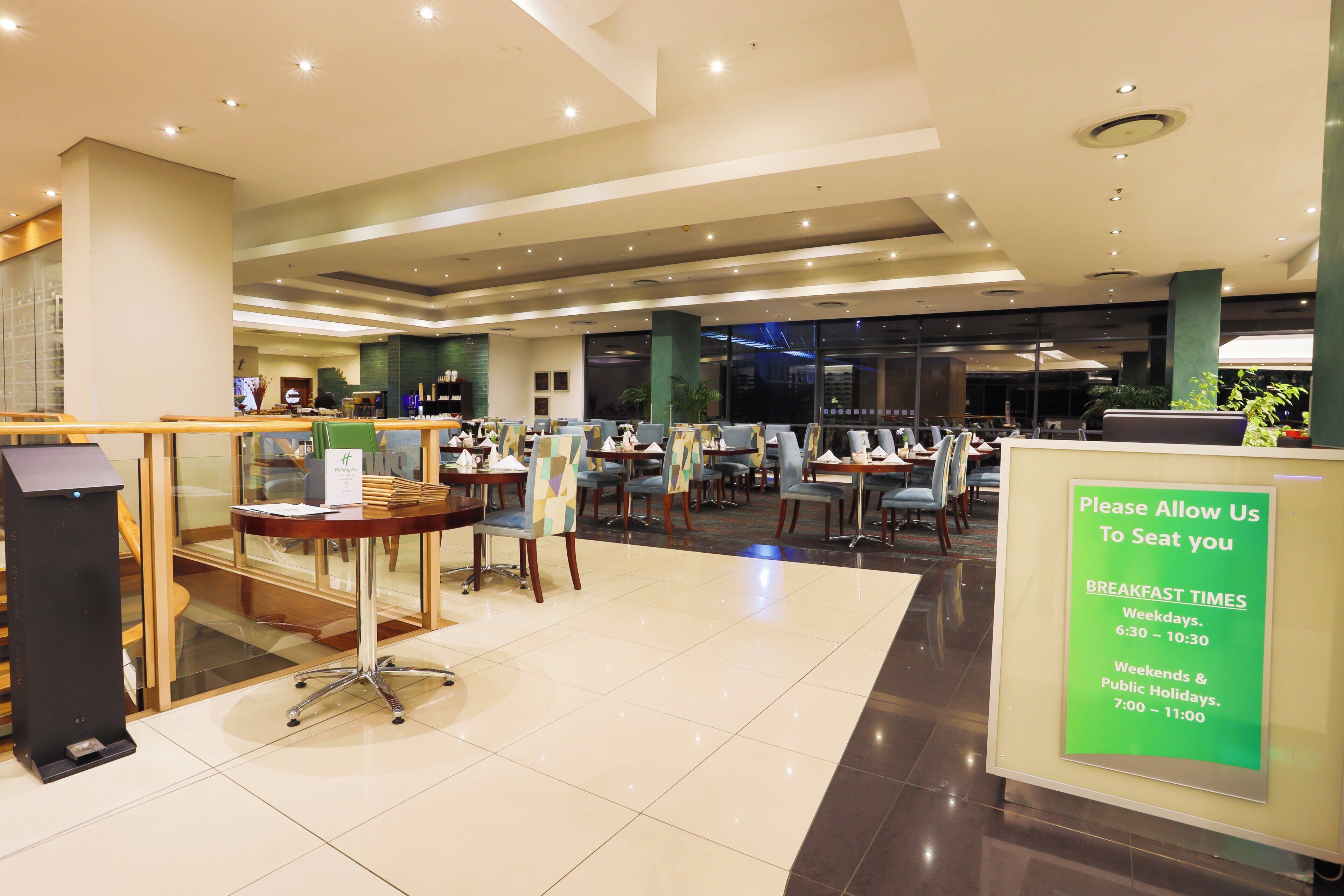 A hotel lobby with a seating area, a reception desk, and a sign indicating breakfast times.