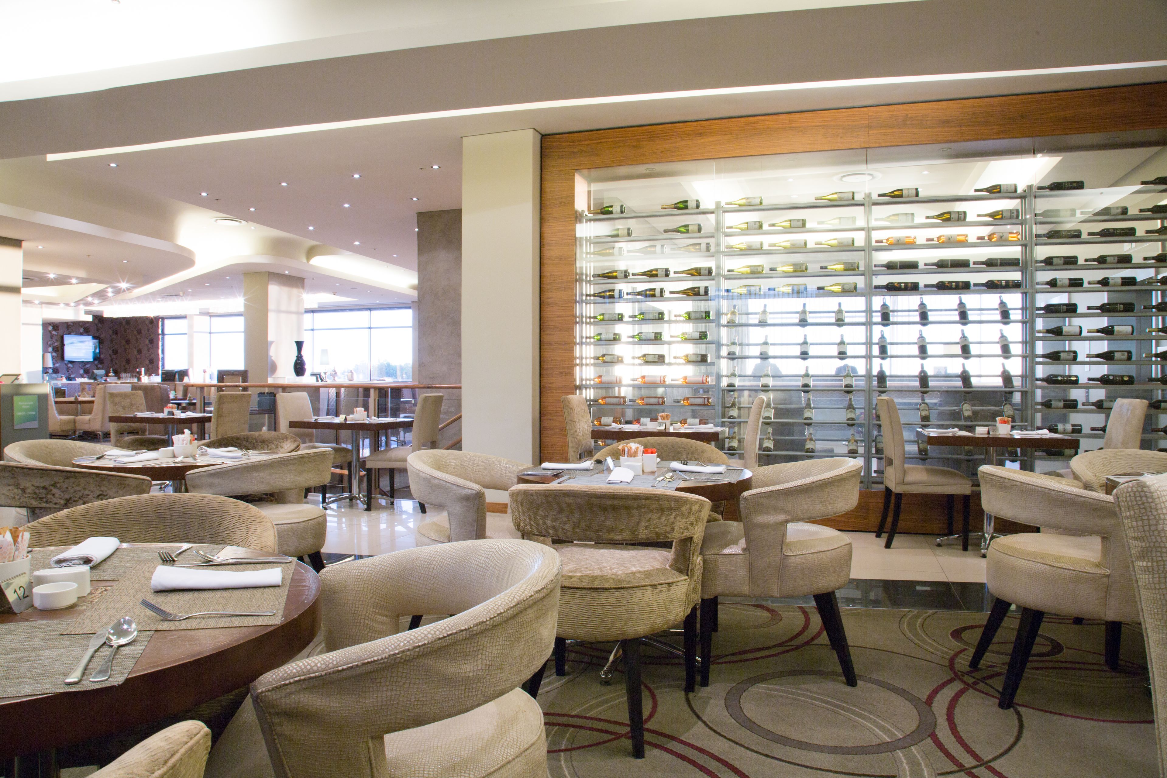A modern hotel lobby with dining areas, a wine display, and comfortable seating.