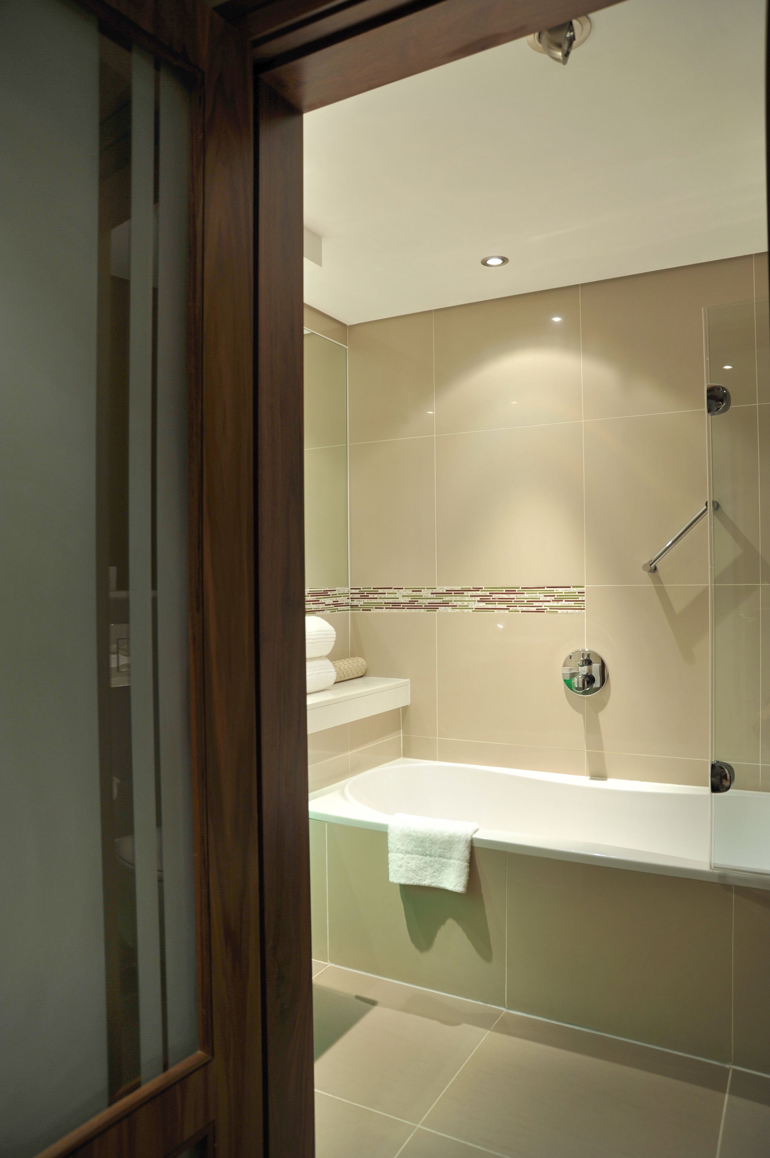A modern bathroom with a glass shower enclosure, a white bathtub, and a beige tiled wall.