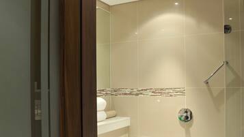 A modern bathroom with a glass shower enclosure, a white bathtub, and a beige tiled wall.