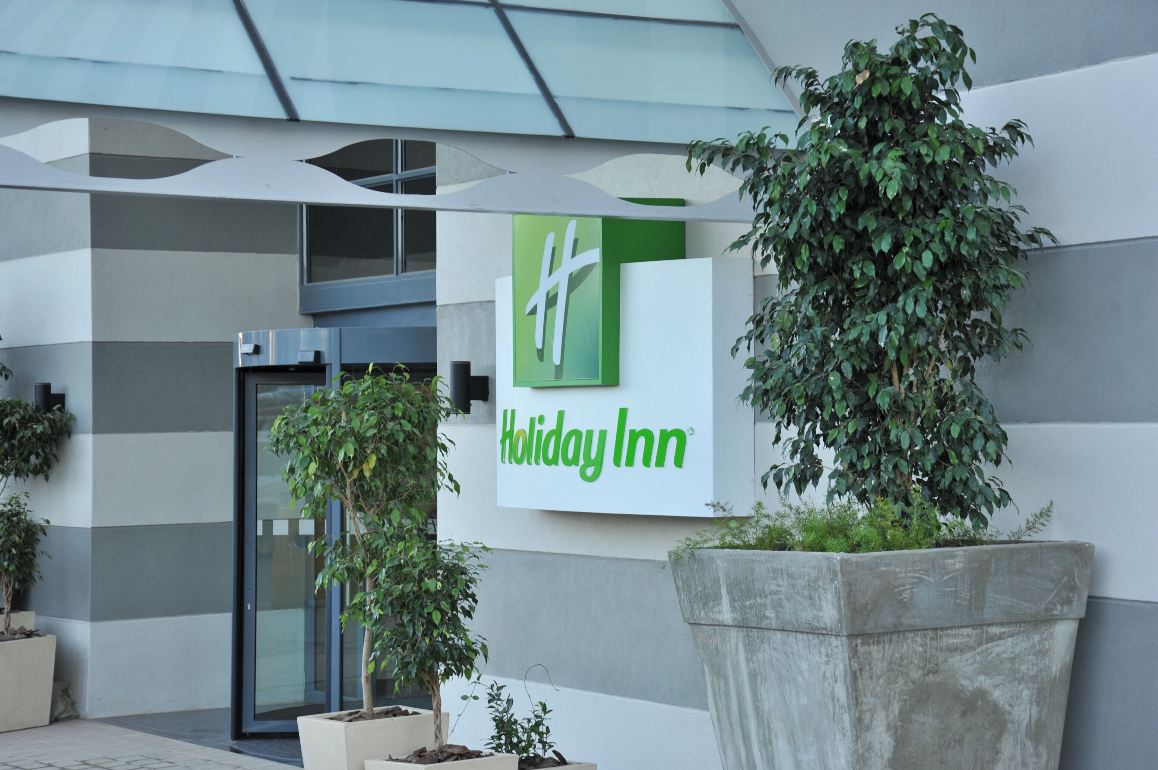 A Holiday Inn sign with a modern building facade and potted plants.