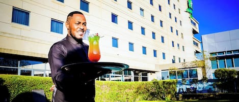 A hotel with a pool, a person holding a tray with a drink, and a building with multiple windows.