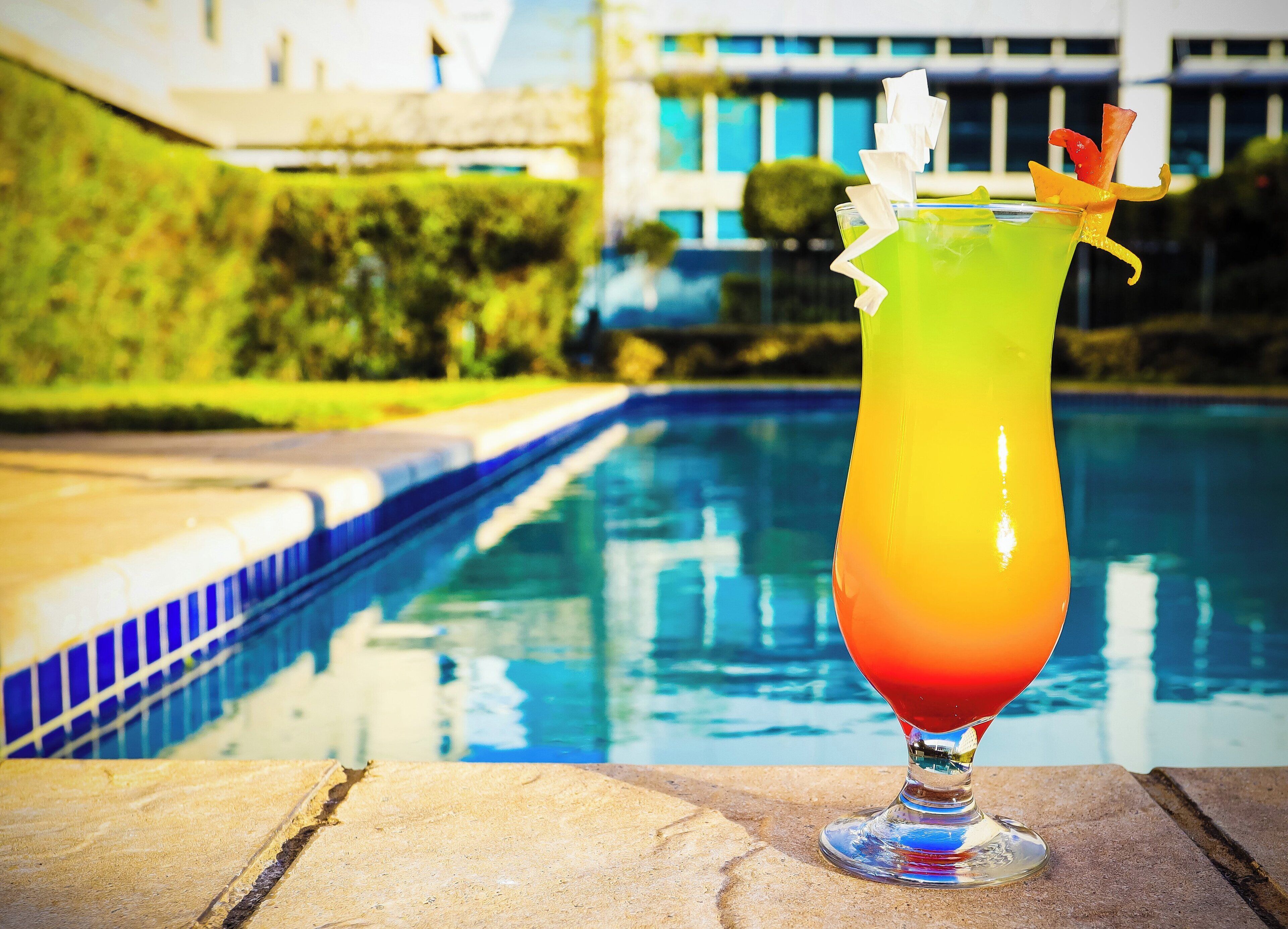 Un vaso de cóctel con un efecto de degradado de color, sobre una superficie de piedra cerca de una piscina.