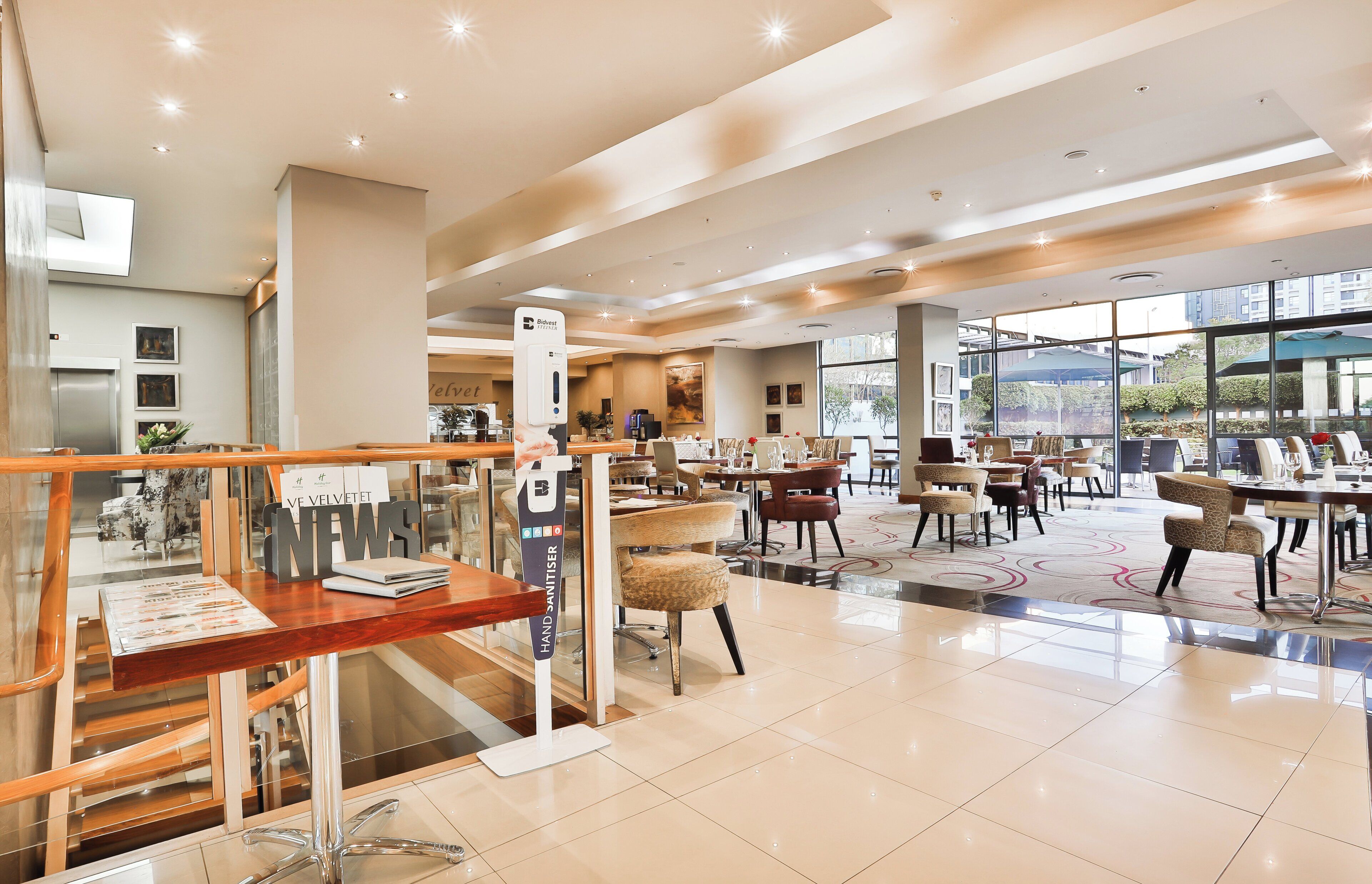 A spacious hotel lobby with a modern design, featuring a reception desk, seating areas, and large windows offering views of the outdoors.