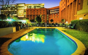 A swimming pool with lounge chairs, surrounded by a well-maintained lawn and a building with multiple floors and large windows.