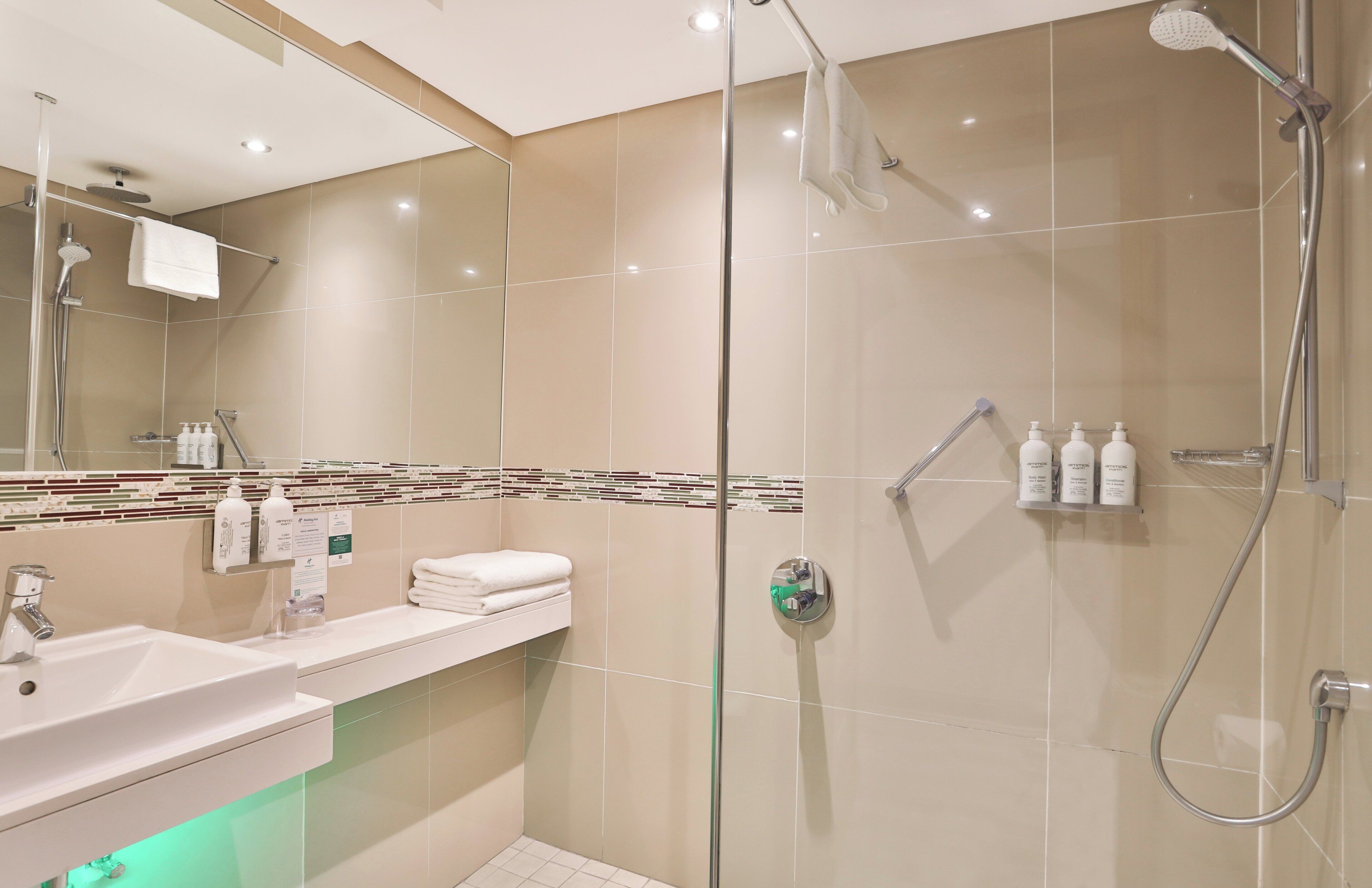 A modern bathroom with a glass-enclosed shower, a sink with a mirror, and toiletries on the wall.