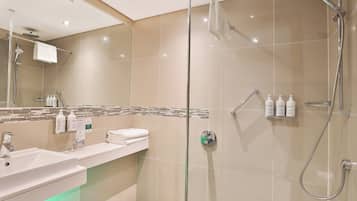 Une salle de bain moderne avec une douche à parois de verre, un lavabo avec un miroir et des articles de toilette fixés au mur.