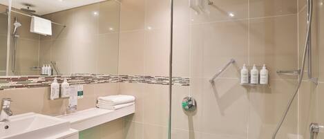 A modern bathroom with a glass-enclosed shower, a sink with a mirror, and toiletries on the wall.