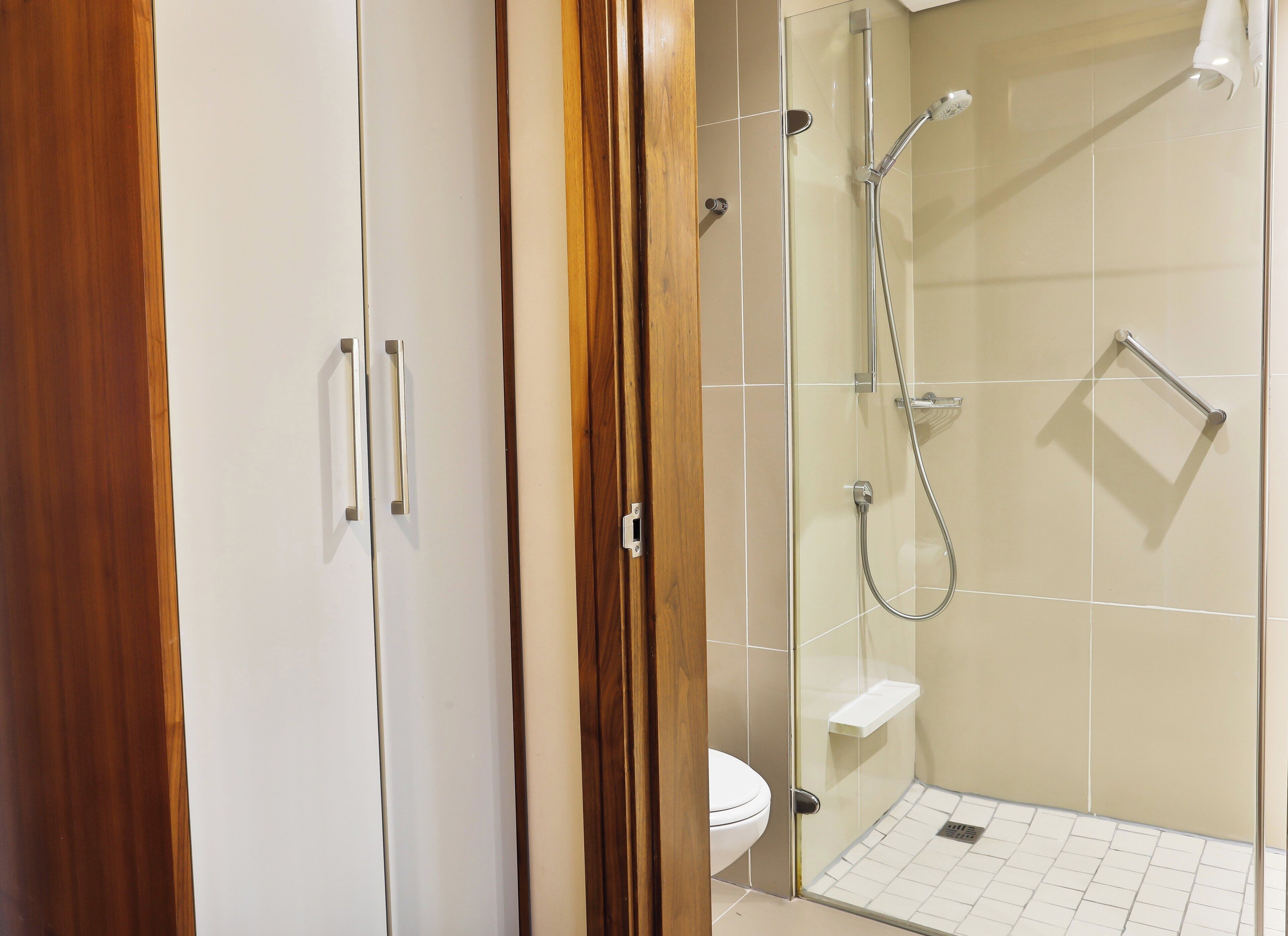 A modern bathroom with a glass-enclosed shower, a toilet, and a wooden wardrobe.